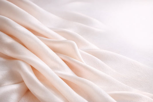 A length of smooth ivory mulberry silk fabric catching soft natural light, its fine even weave and subtle sheen visible