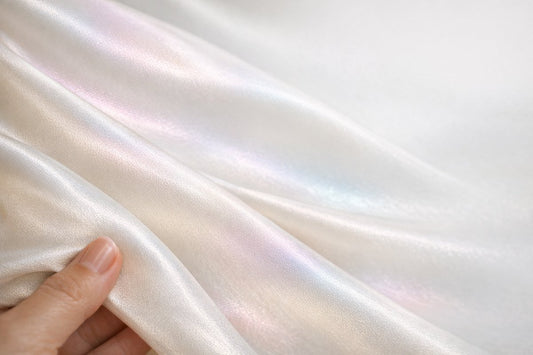 A close-up of ivory mulberry silk fabric held to the light, its colour-shifting sheen and fine weave revealing it as real silk