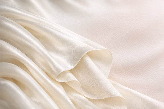 A close-up of ivory silk charmeuse folded back on itself, showing its glossy lustrous front face and softer matte reverse