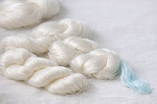Skeins of pearly-white raw mulberry silk thread in soft natural light, their long even fibres and clean lustre visible