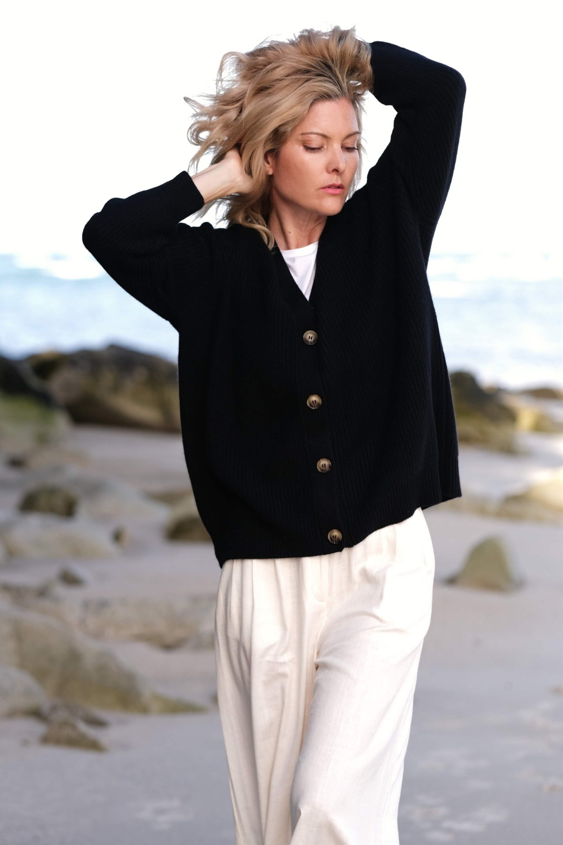 Woman in black cashmere cardigan with hand in hair at beach – Love Cashmere NZ