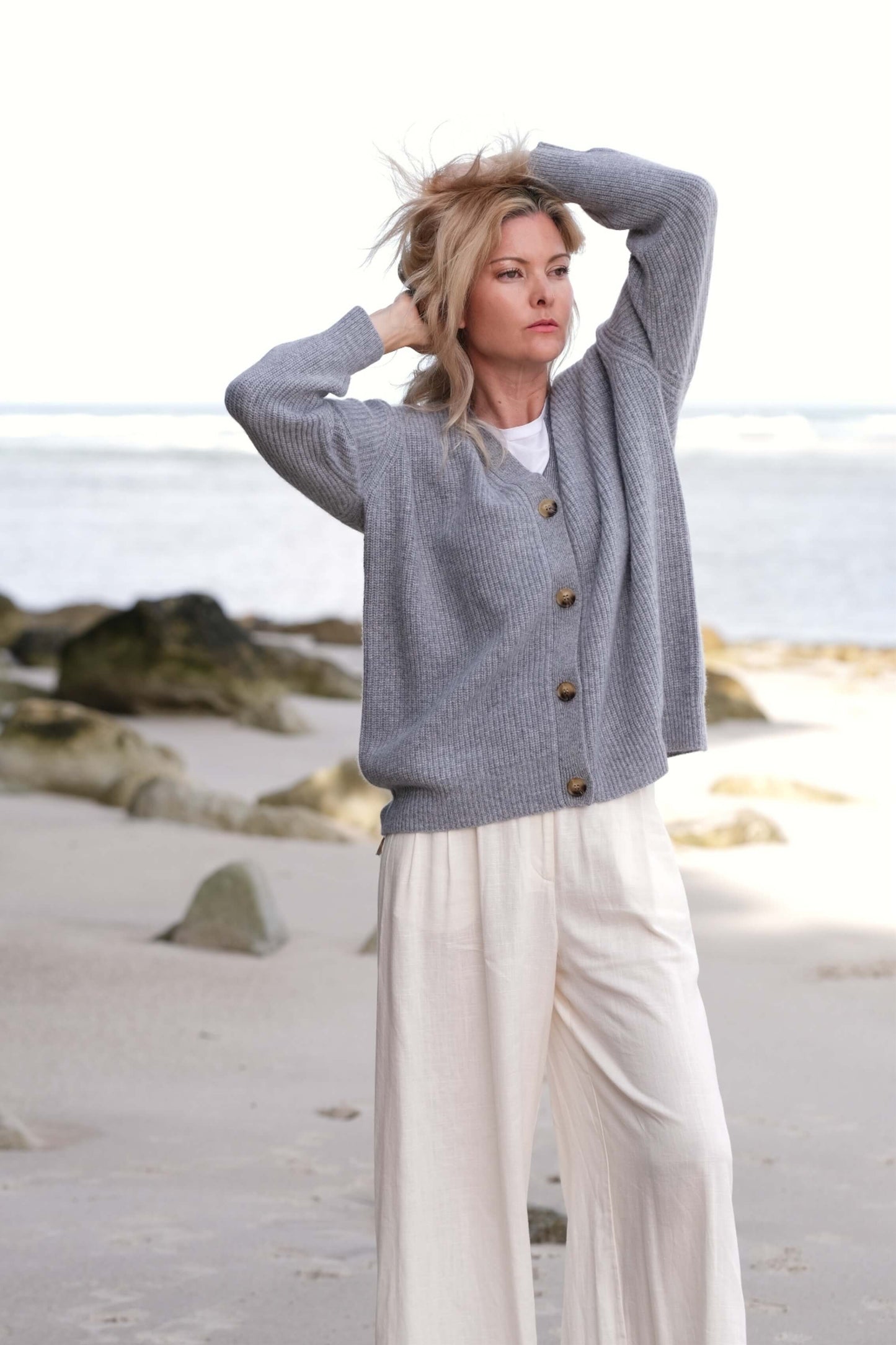 Woman at the beach in grey cashmere cardigan, arm raised – Love Cashmere NZ
