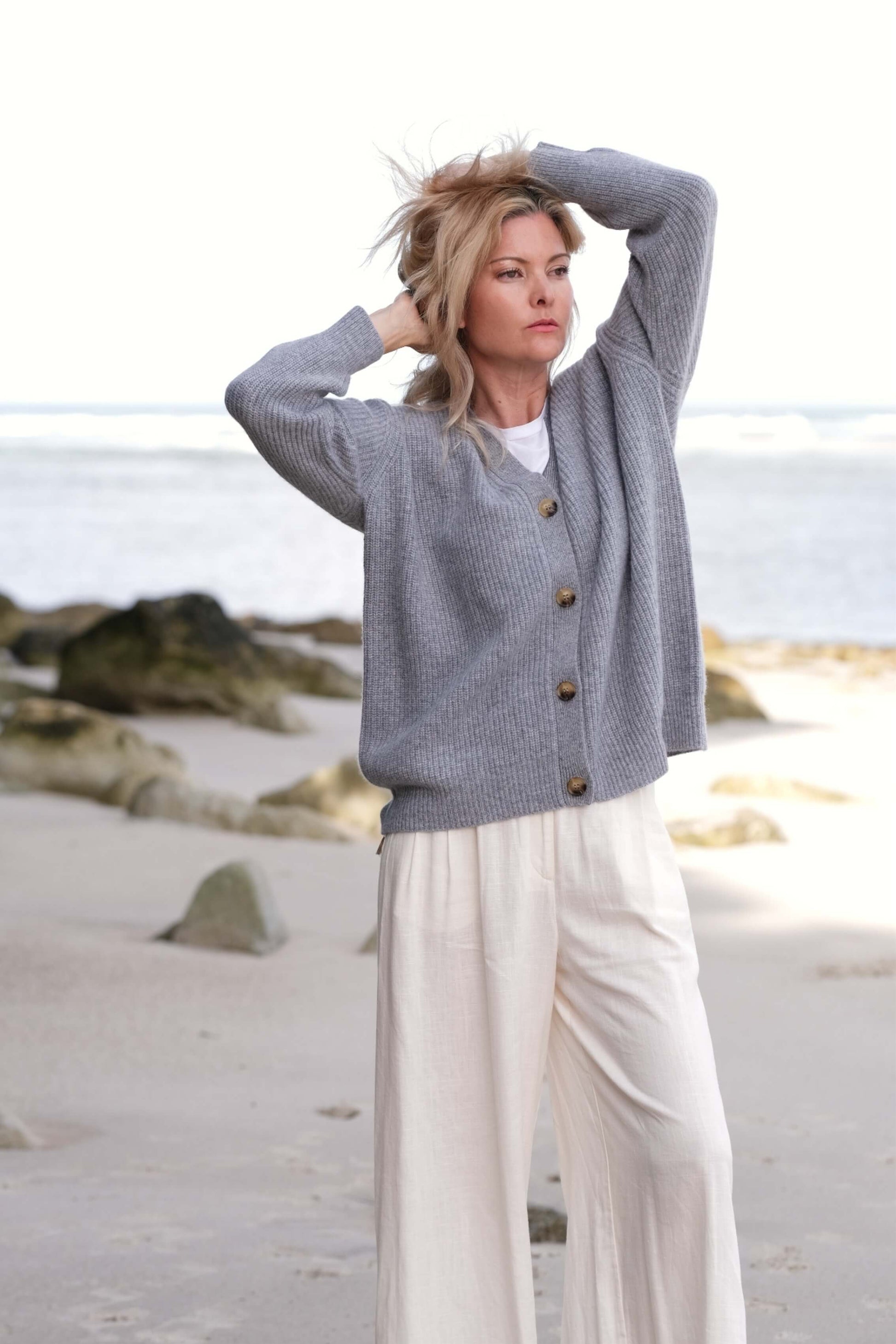 Woman at the beach in grey cashmere cardigan, arm raised – Love Cashmere NZ