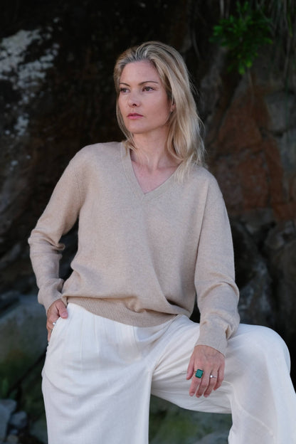 Woman at dusk beach in beige cashmere V-neck and white pants – Love Cashmere NZ