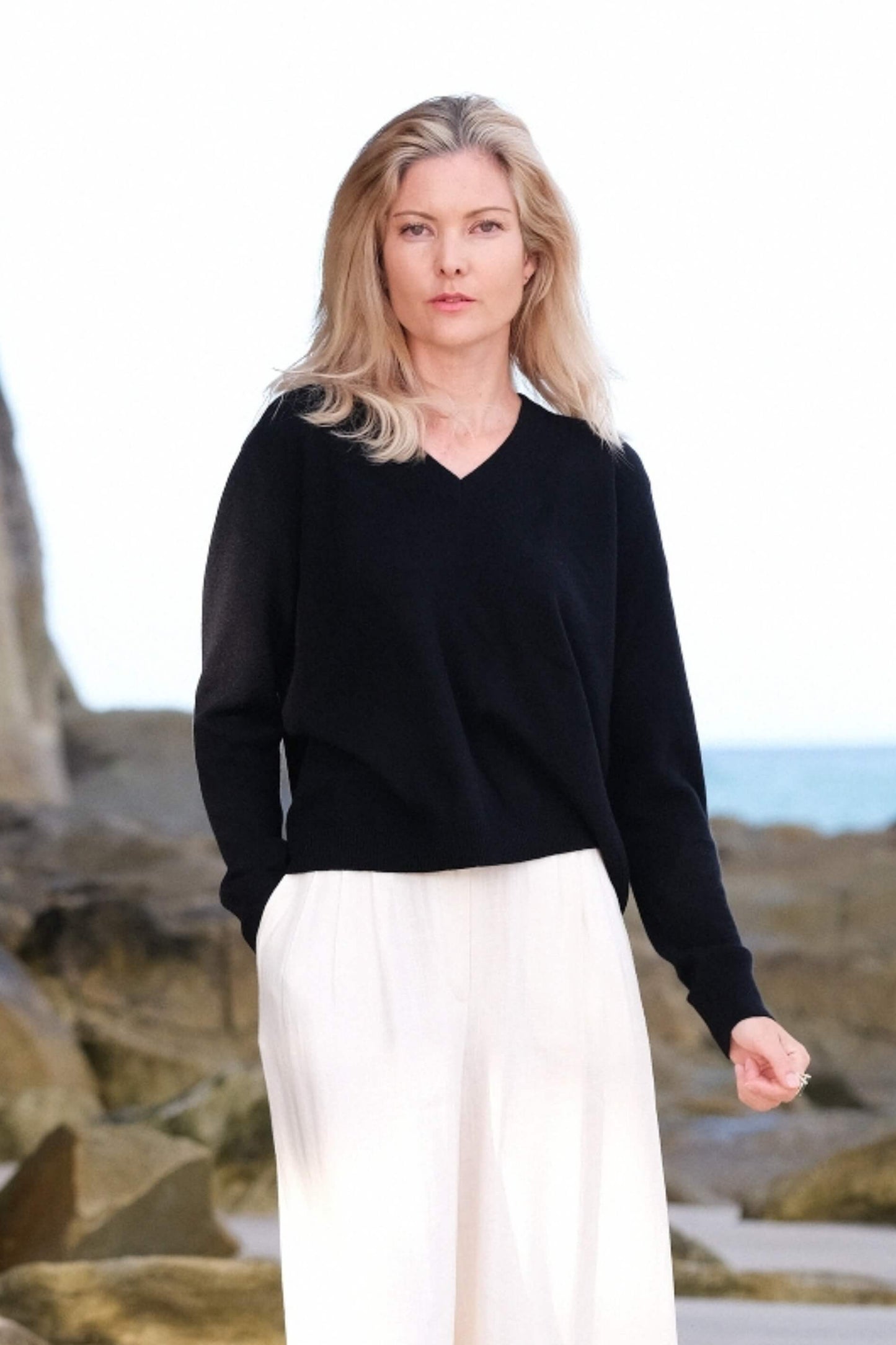 Woman at the beach in black cashmere V-neck and white pants – Love Cashmere NZ