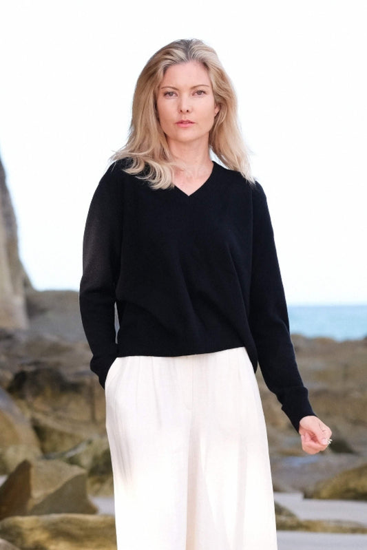 Woman at the beach in black cashmere V-neck and white pants – Love Cashmere NZ