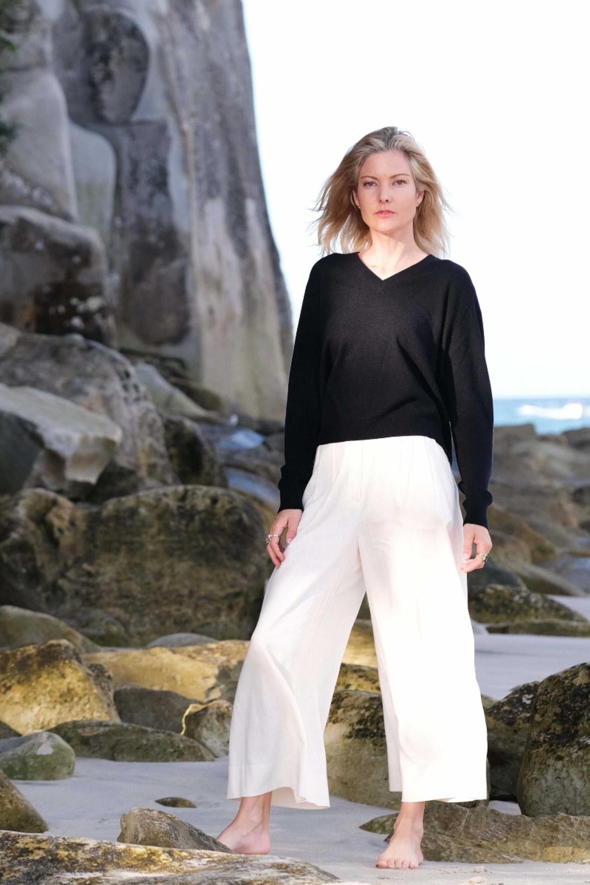 Full-length look in black cashmere V-neck on coastal rocks – Love Cashmere NZ