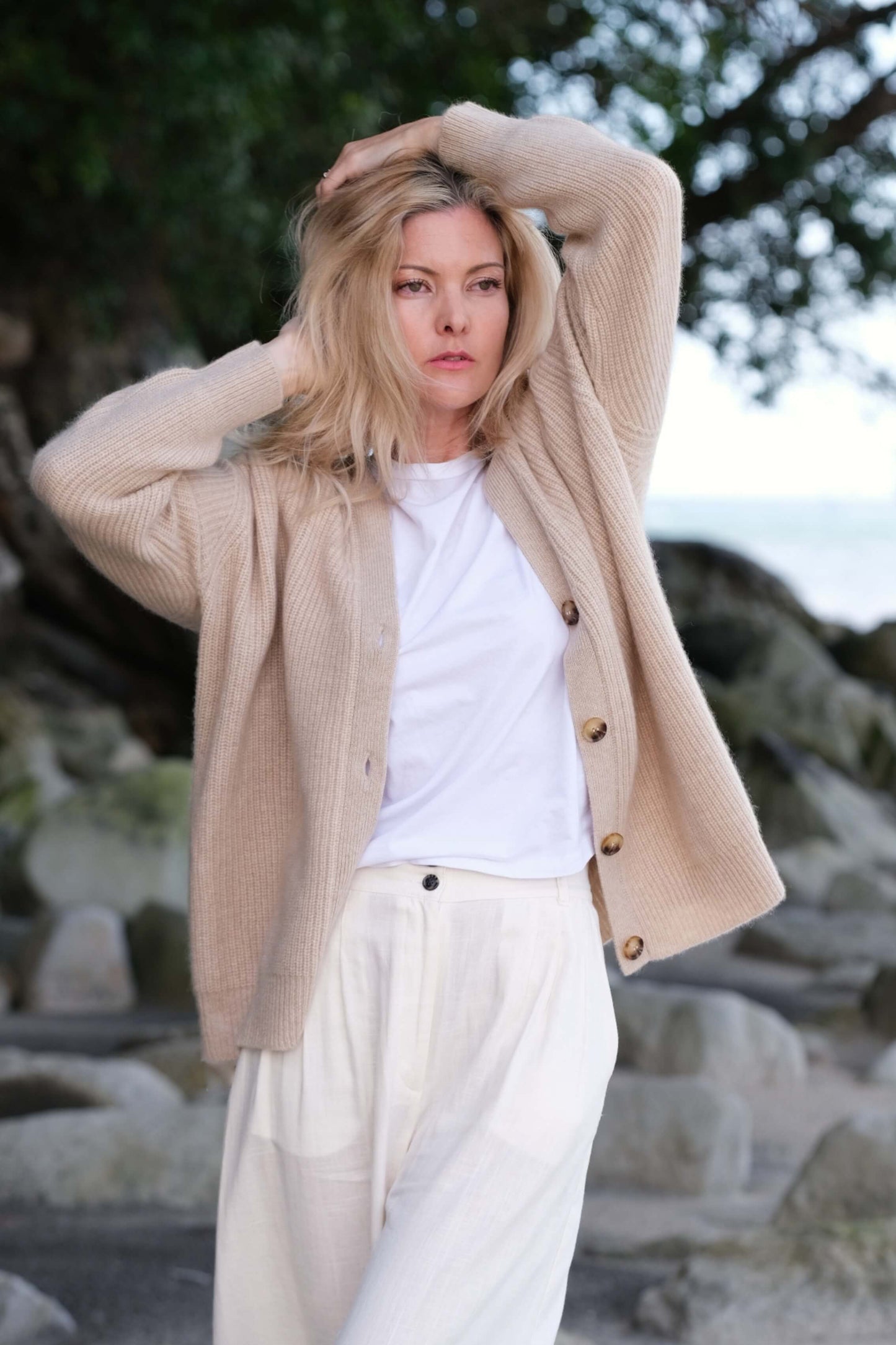 Woman at the beach in beige cashmere cardigan, arm raised – Love Cashmere NZ