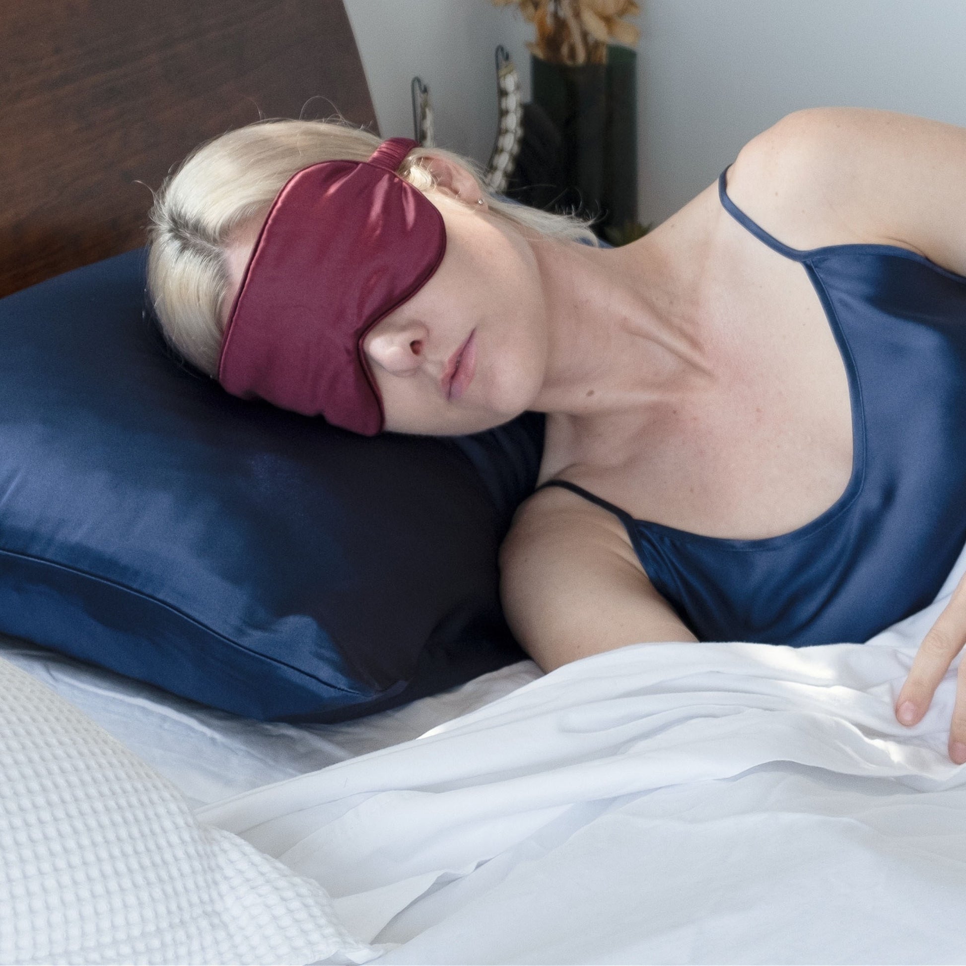 Woman sleeping on navy silk pillowcase wearing a burgundy silk eye mask – LS Silk NZ