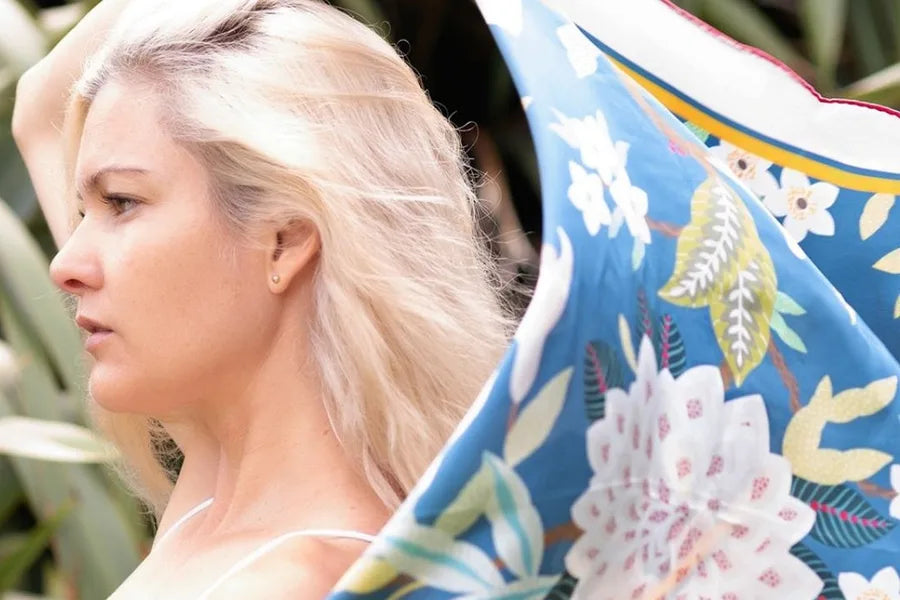 A woman holding up a blue silk scarf printed with large white and pink flowers
